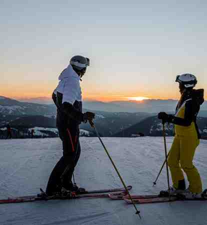 Due persone con gli sci guardano il tramonto